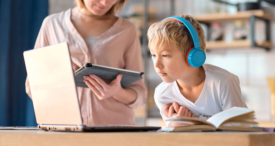 Photo of a young student leaning in to learn on a laptop device with blue headphones on