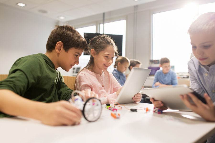 Photo of smiling children at a table learning from an electronic tablet device