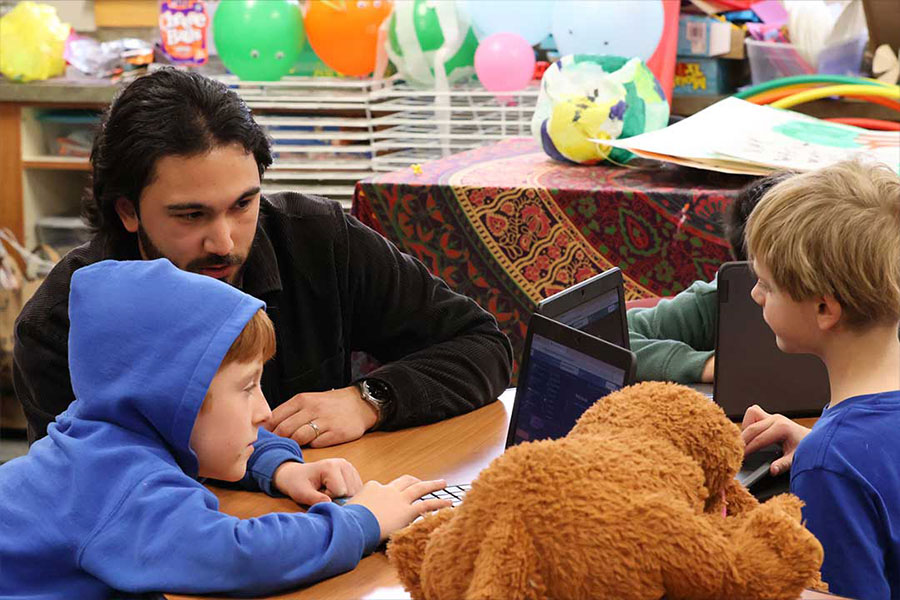 three kids working on computers with a male teacher helping