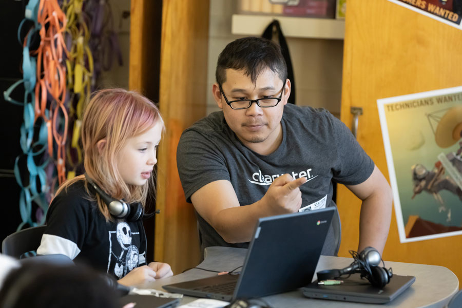 Photo of an educator assisting a young school student on a laptop